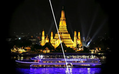River cruise boat with illuminated Wat Arun temple in Bangkok at night.