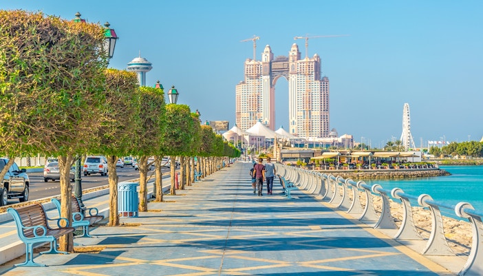 People walking along the Corniche in Abu Dhabi with city skyline in the background.