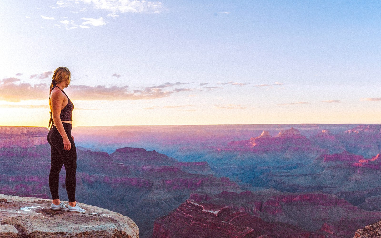 Person standing at Grand Canyon South Rim during sunset.