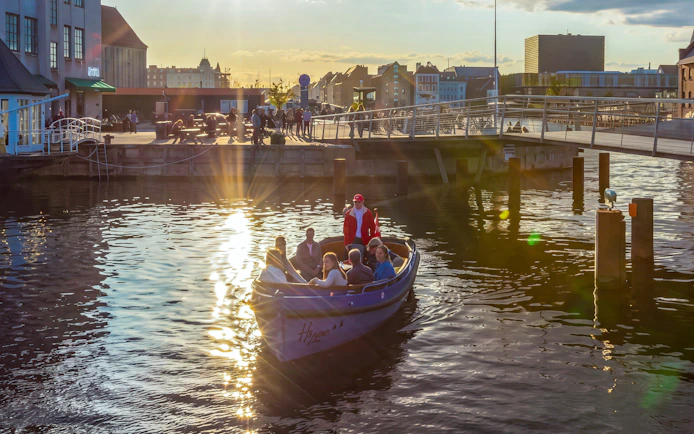 Canal boat tour in Copenhagen at sunset with passengers enjoying the view.