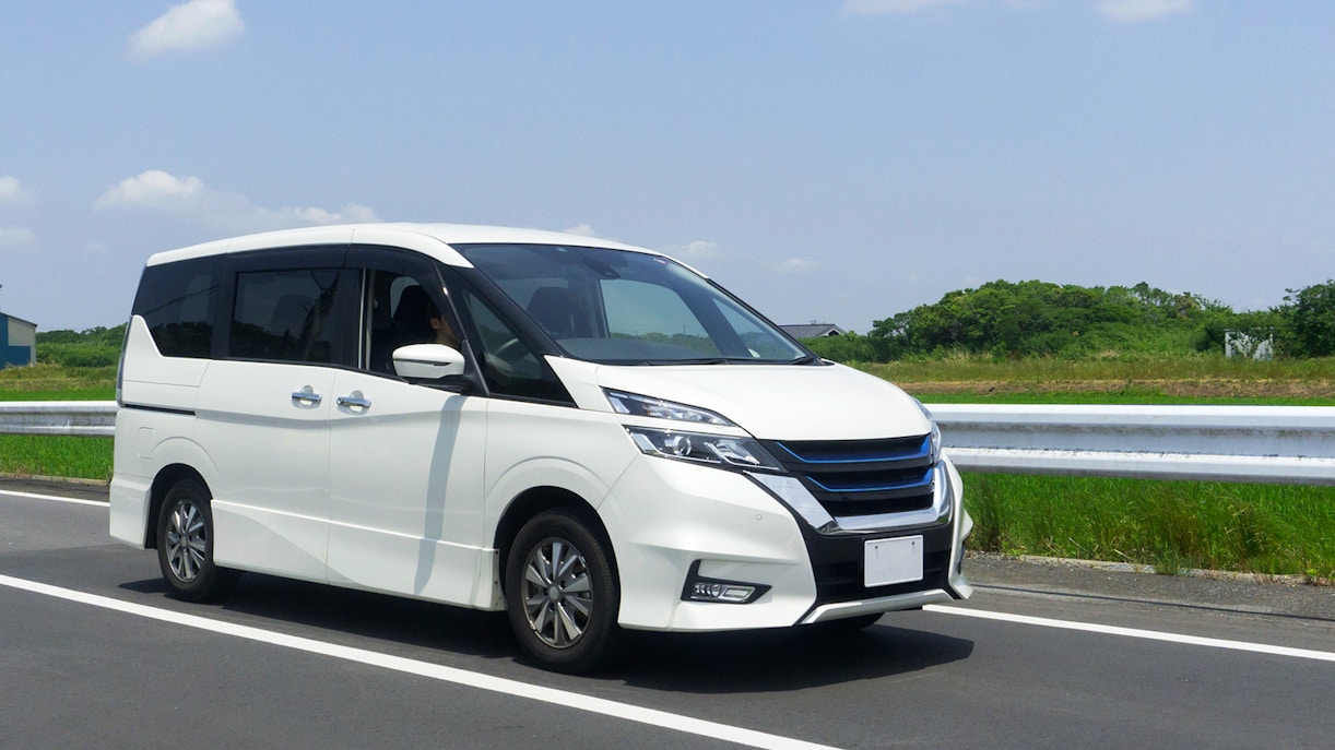 Minivan driving on a highway with green fields in the background.