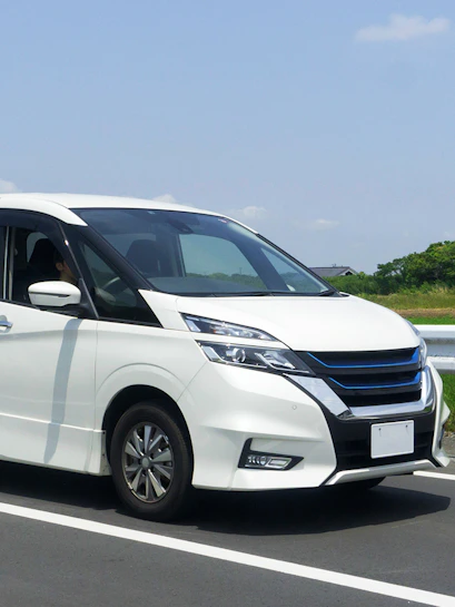 Minivan driving on a highway with green fields in the background.