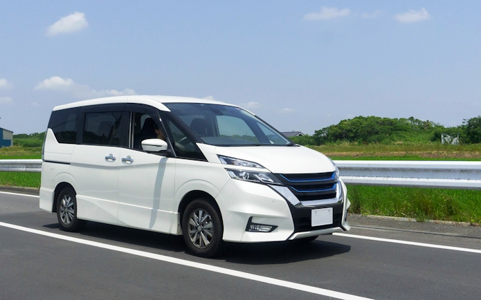 Minivan driving on a highway with green fields in the background.