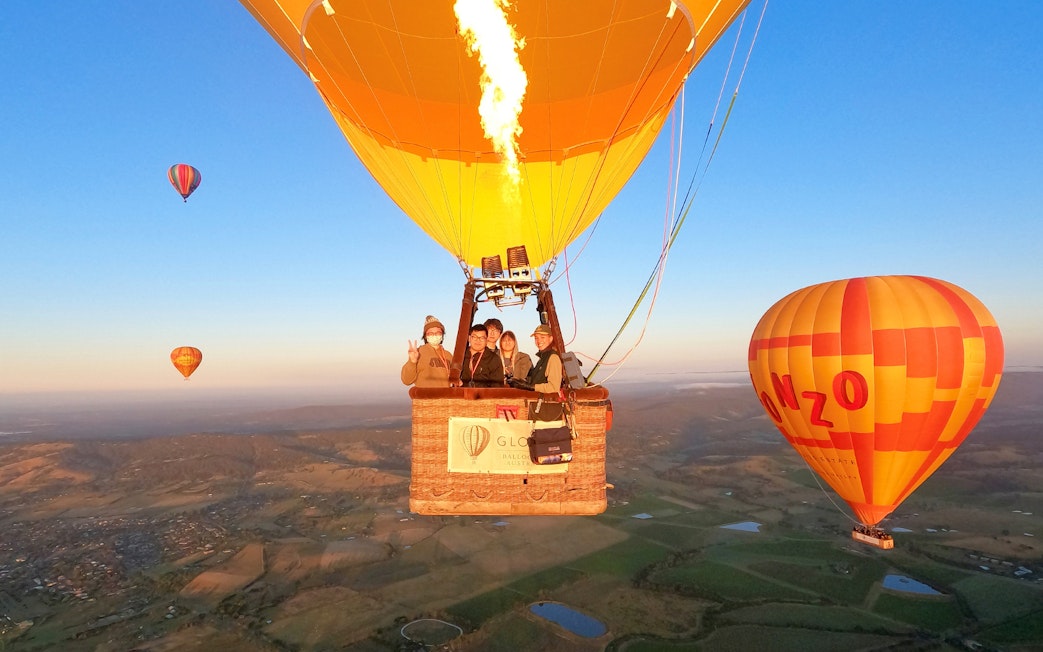 Hot air balloons floating over Yarra Valley at sunrise with passengers enjoying the view.