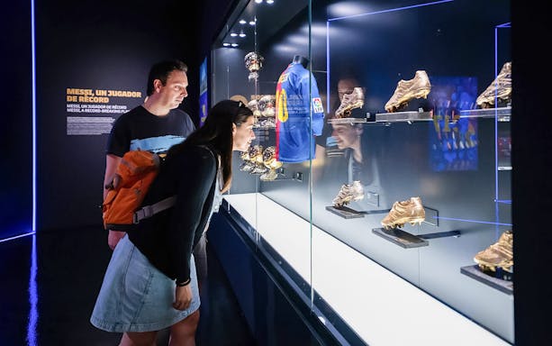 Visitors viewing FC Barcelona memorabilia display with Messi's jersey and golden boots.