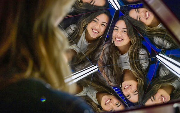 Reflections of a smiling woman in a mirrored exhibit at The TUBE.