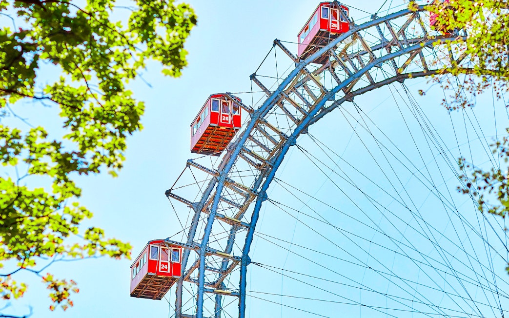 Red cabins on the Vienna Giant Ferris Wheel, Austria, with blue sky and green leaves.