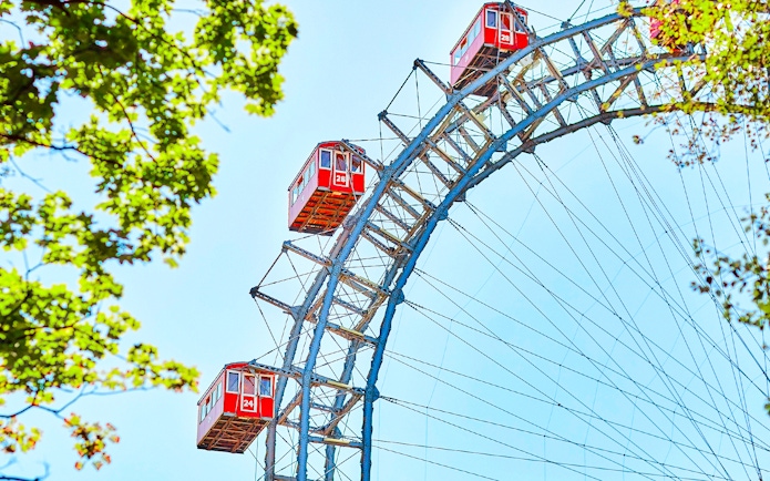 Red cabins on the Vienna Giant Ferris Wheel, Austria, with blue sky and green leaves.