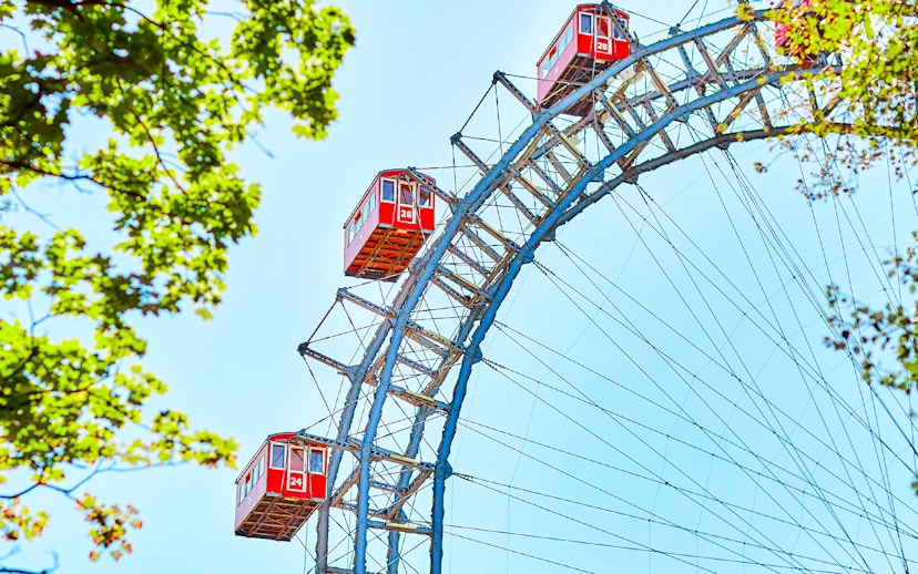 Red cabins on the Vienna Giant Ferris Wheel, Austria, with blue sky and green leaves.