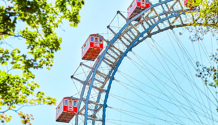 Red cabins on the Vienna Giant Ferris Wheel, Austria, with blue sky and green leaves.
