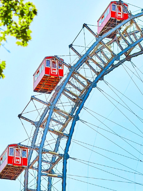 Red cabins on the Vienna Giant Ferris Wheel, Austria, with blue sky and green leaves.