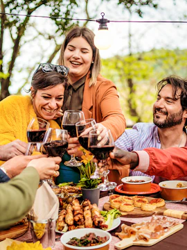 Friends toasting with wine at outdoor dinner party with tapas in Barcelona.