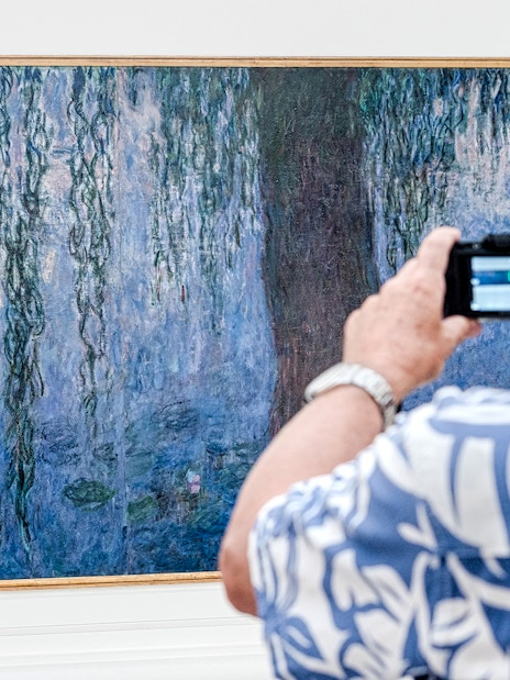 Tourist photographing Monet painting at Orangerie Museum, Paris.