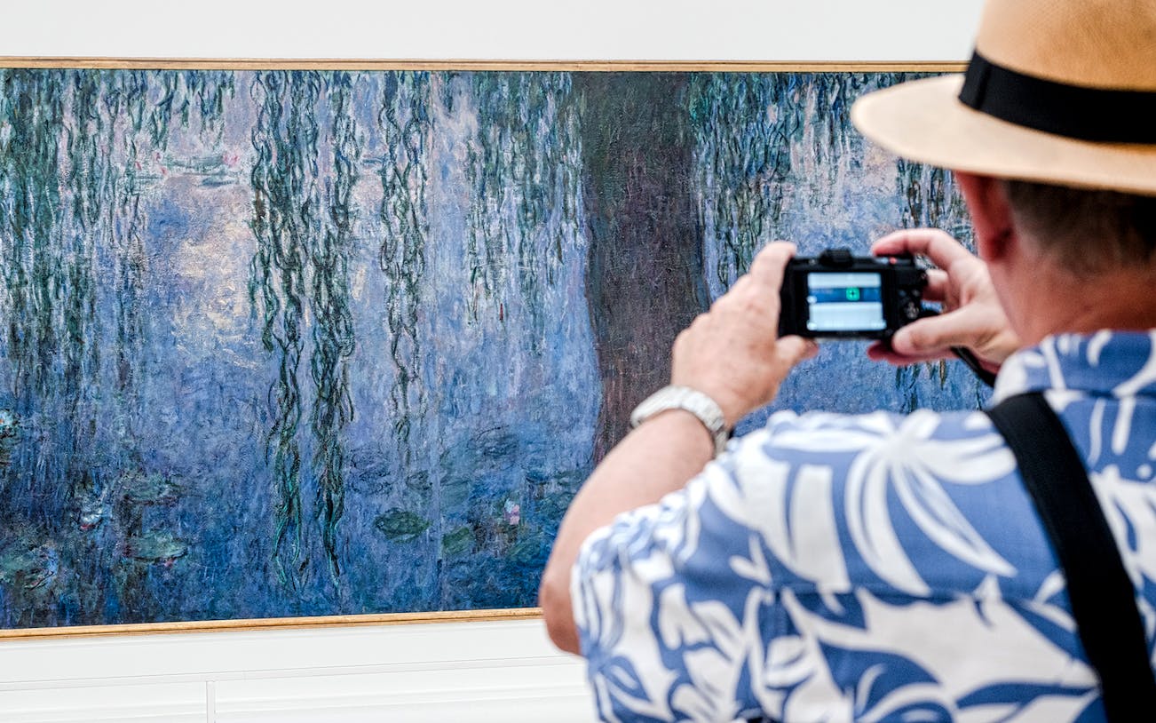 Tourist photographing Monet painting at Orangerie Museum, Paris.