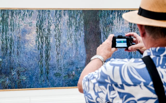 Tourist photographing Monet painting at Orangerie Museum, Paris.