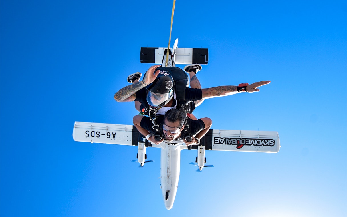 Skydiver tandem jumping from plane in Dubai against clear blue sky.