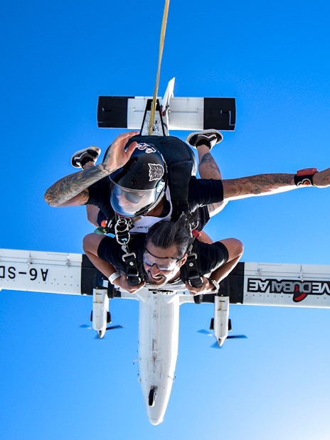Skydiver tandem jumping from plane in Dubai against clear blue sky.