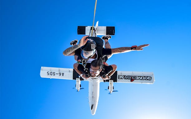 Skydiver tandem jumping from plane in Dubai against clear blue sky.