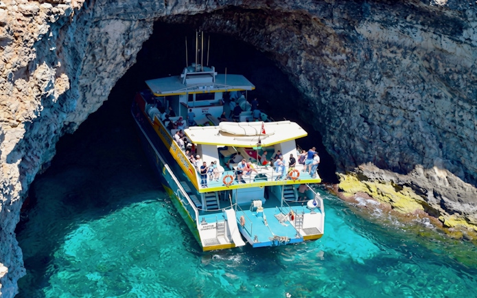 Tourist boat entering cave at Blue Lagoon, Malta.