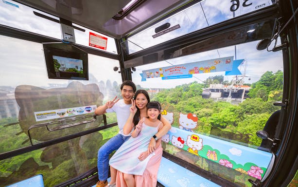 Family enjoying a ride in the Hello Kitty-themed Singapore Cable Car with lush greenery outside.