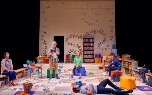 Actors performing a scene from "Eureka Day" in a colorful classroom setting.