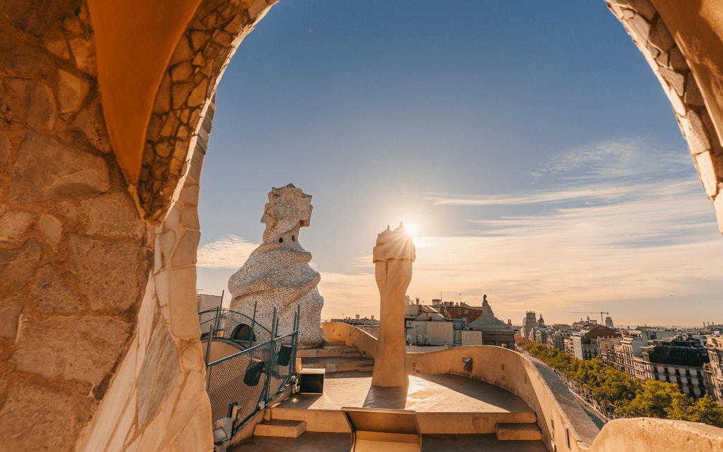La Pedrera Casa Mila terrace view at sunrise, Barcelona skyline in background.