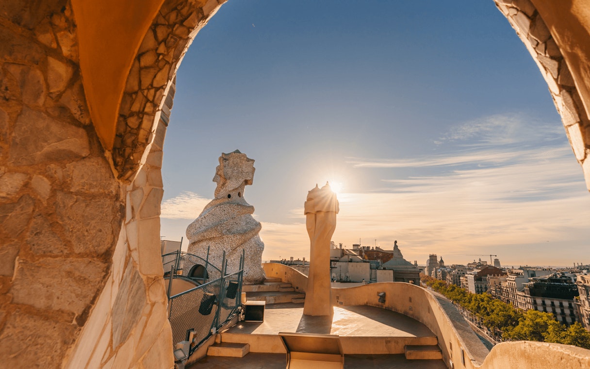 La Pedrera Casa Mila terrace view at sunrise, Barcelona skyline in background.