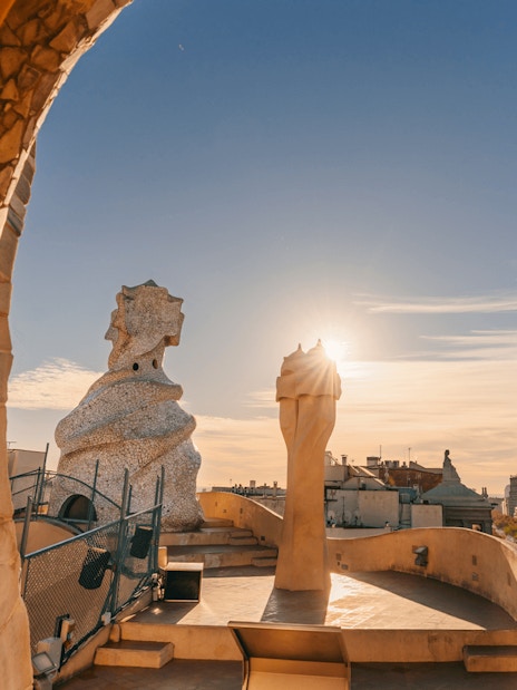 La Pedrera Casa Mila terrace view at sunrise, Barcelona skyline in background.