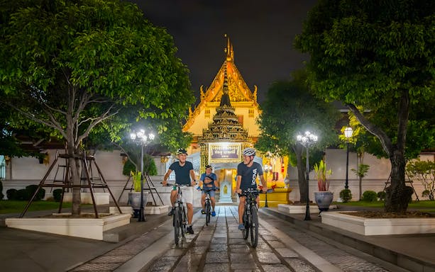 Cyclists on a guided night tour in Bangkok, riding past a lit temple.