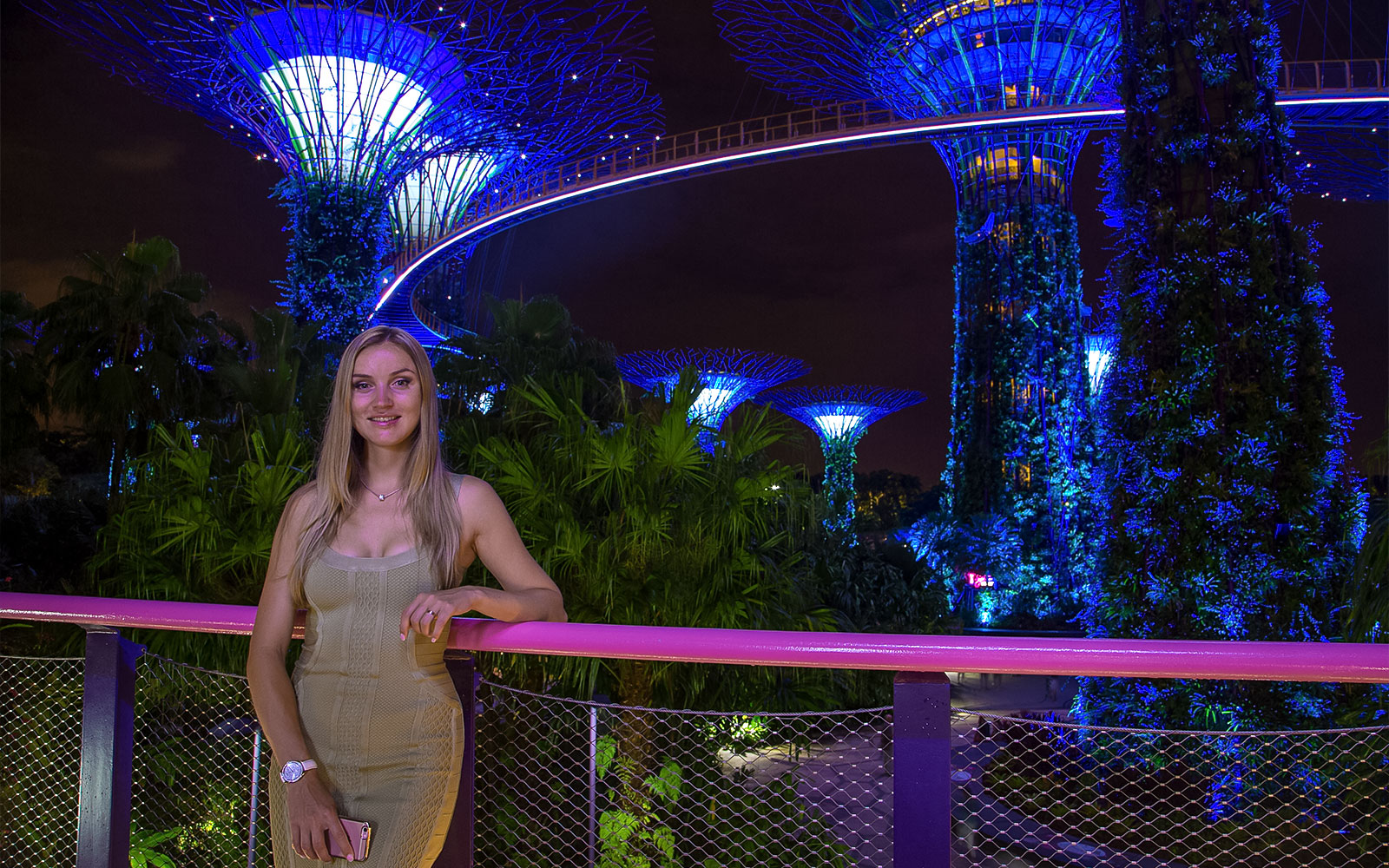 Person posing at night in front of illuminated Supertree Grove, Gardens by the Bay, Singapore.
