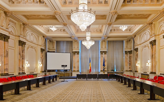Palace of Parliament conference room with chandeliers and Romanian flags.