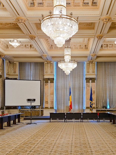 Palace of Parliament conference room with chandeliers and Romanian flags.