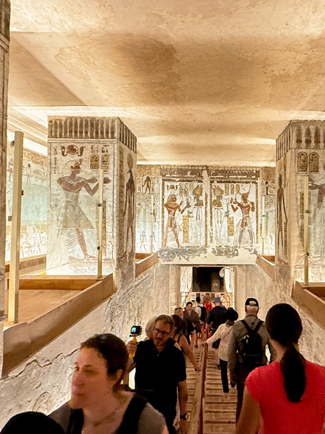 Visitors exploring the Valley of the Kings tomb with ancient Egyptian wall art.