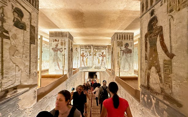 Visitors exploring the Valley of the Kings tomb with ancient Egyptian wall art.