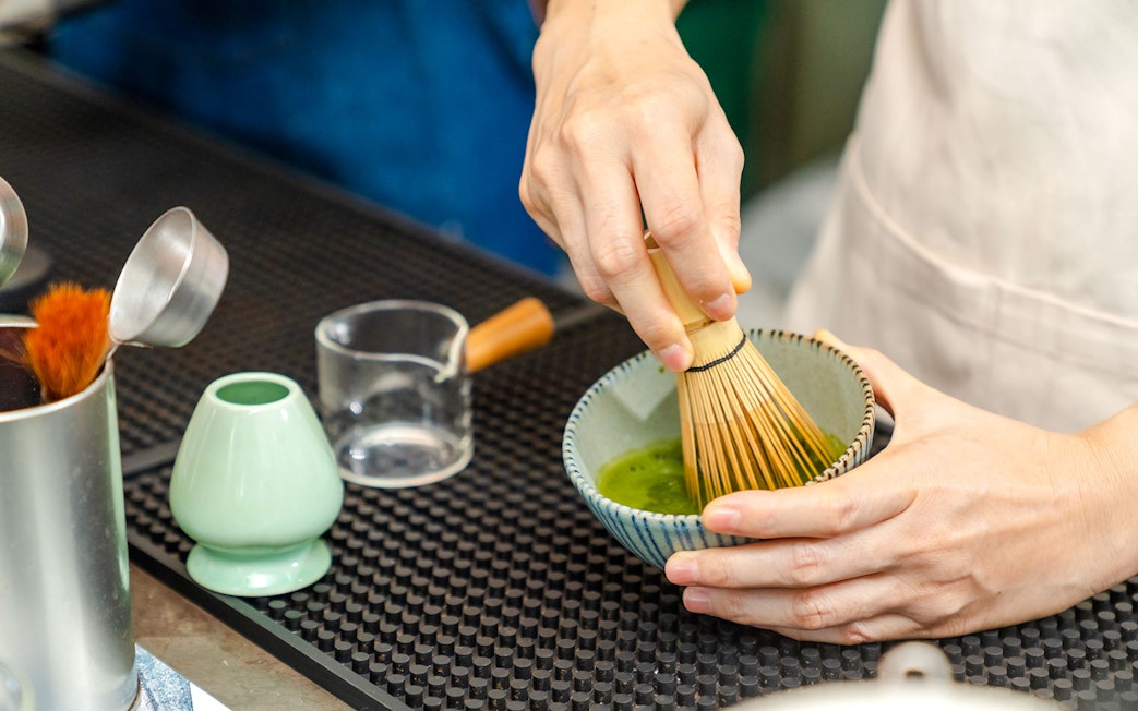 Barista whisking matcha green tea in a bowl.