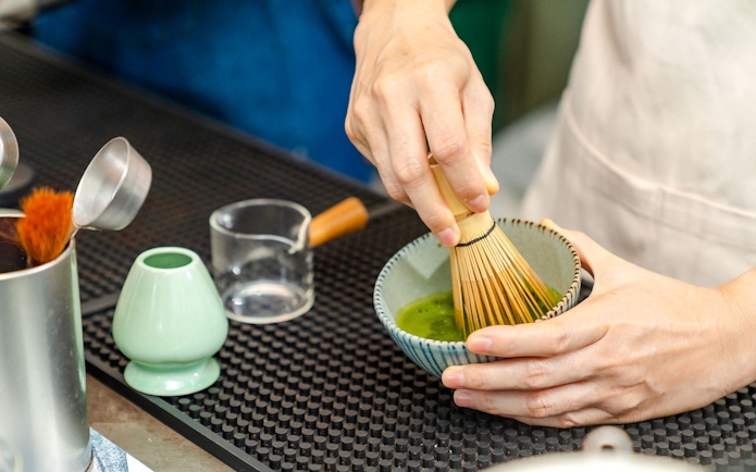 Barista whisking matcha green tea in a bowl.