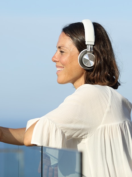 Woman listening to audio guide on ship with earphones, holding smartphone.