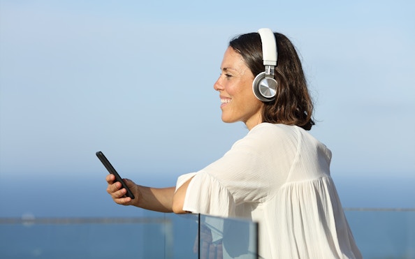 Woman listening to audio guide on ship with earphones, holding smartphone.