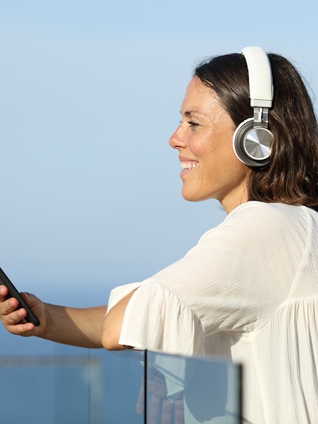 Woman listening to audio guide on ship with earphones, holding smartphone.