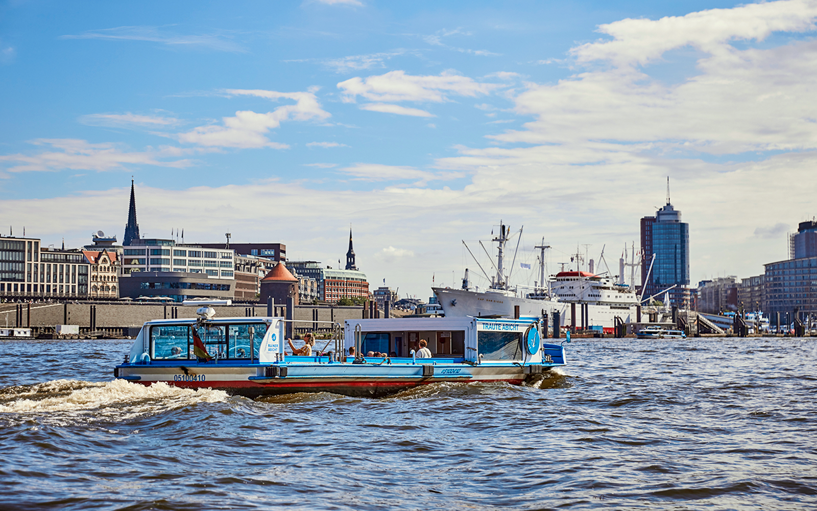 Tour boat cruising through Hamburg harbor with city skyline in background.
