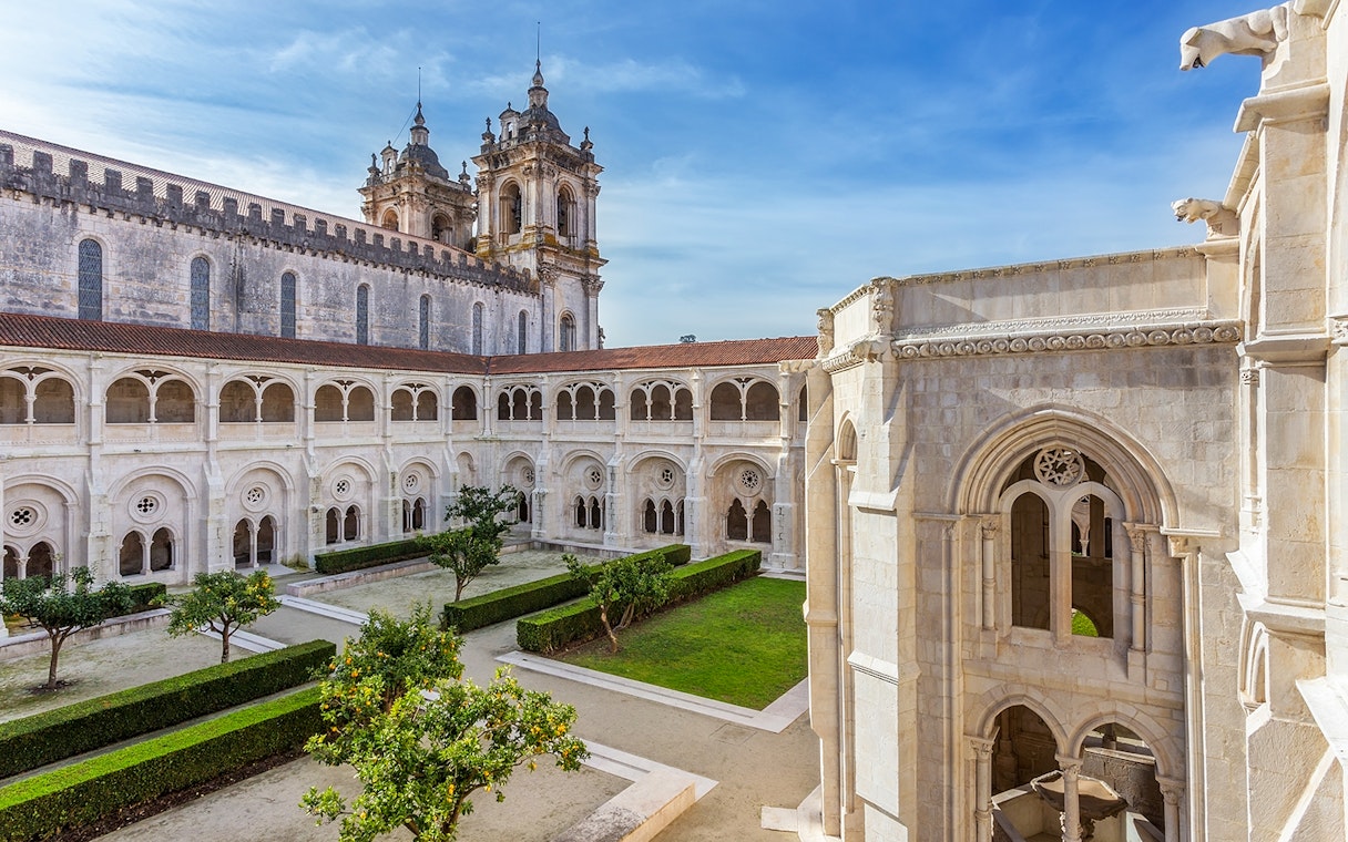 Alcobaça Monastery courtyard with Gothic architecture and manicured gardens in Portugal.