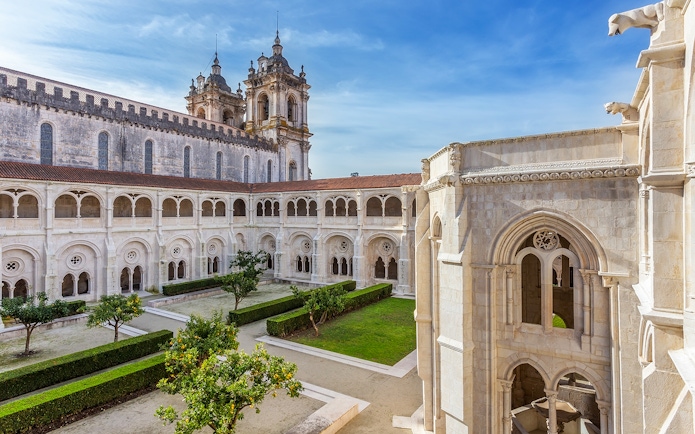 Alcobaça Monastery courtyard with Gothic architecture and manicured gardens in Portugal.