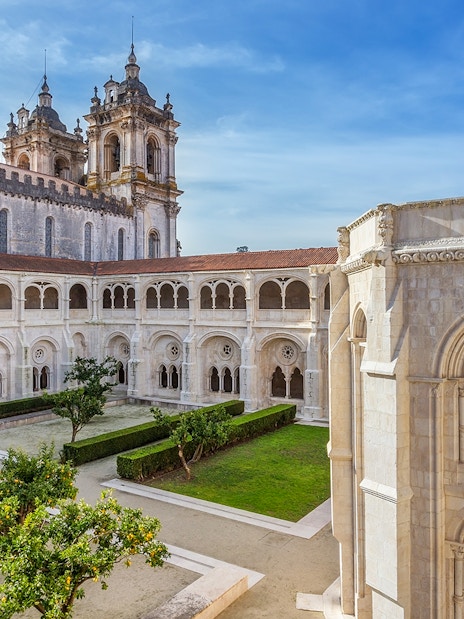 Alcobaça Monastery courtyard with Gothic architecture and manicured gardens in Portugal.