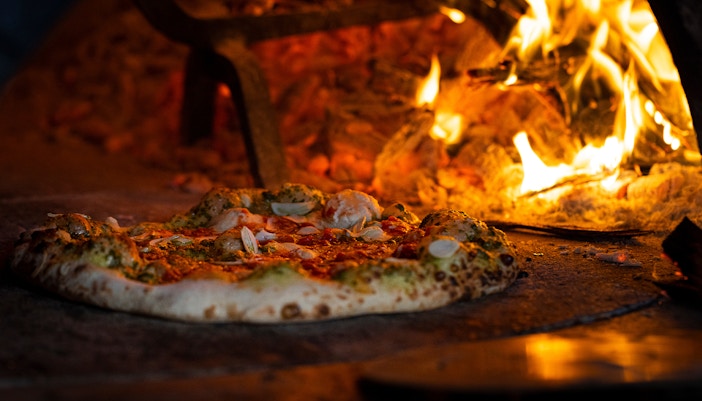 Woodfire pizza baking in a traditional oven with flames.