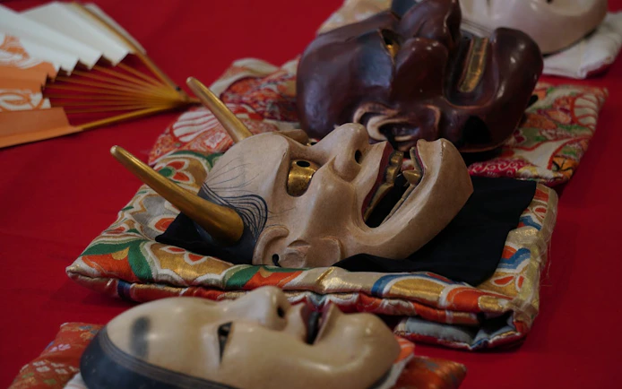 Noh theater masks on colorful fabric in Kyoto workshop.