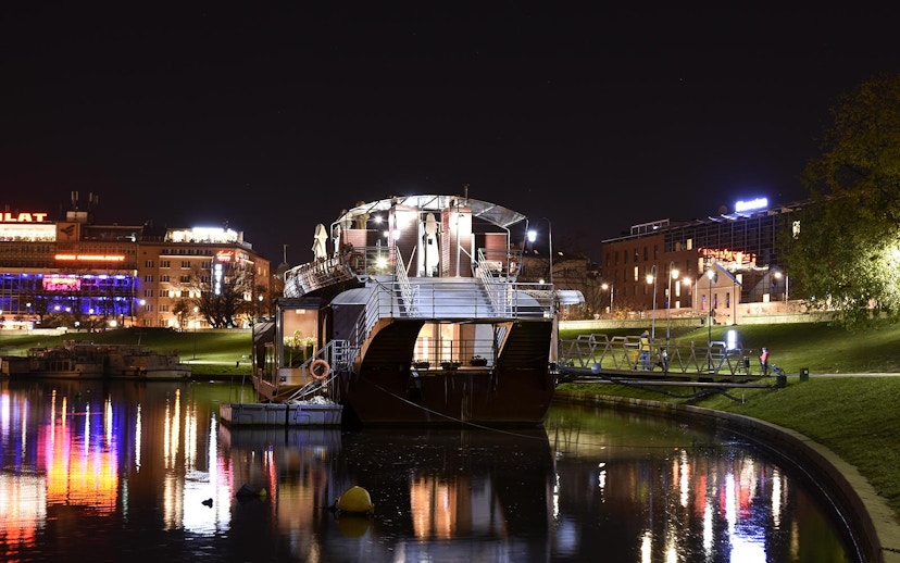 Night view of a boat docked on the Vistula River with city lights reflecting on the water.