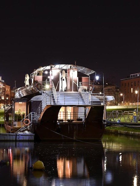 Night view of a boat docked on the Vistula River with city lights reflecting on the water.