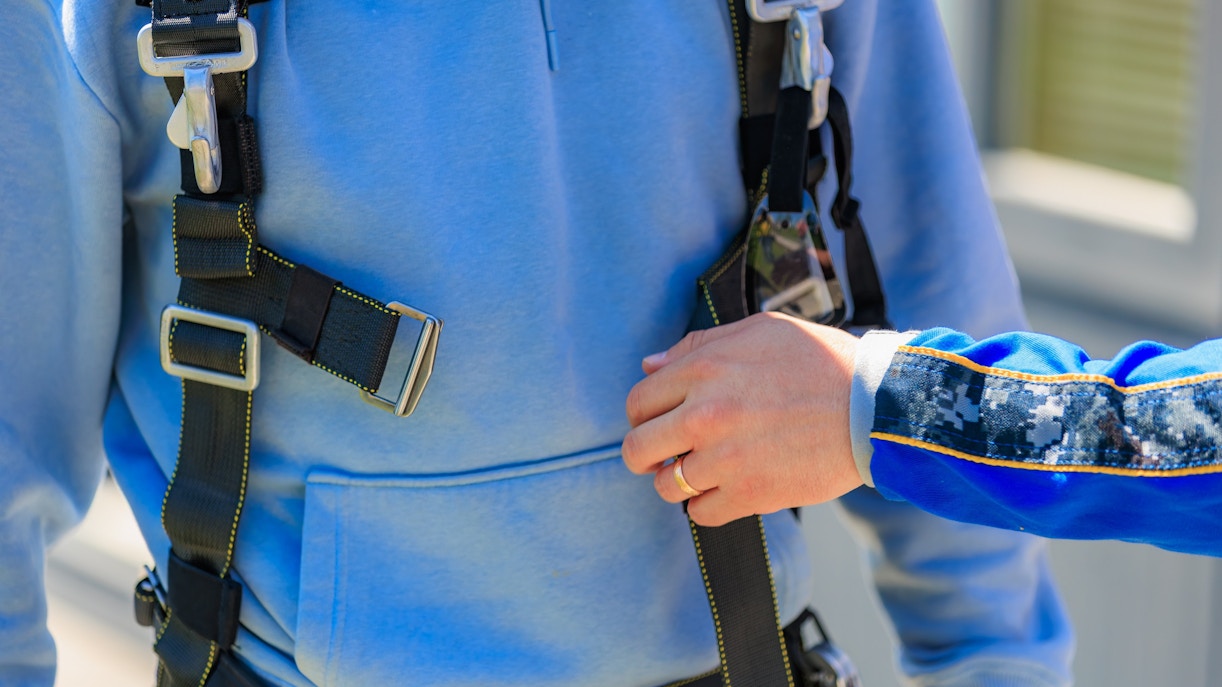 Man securing harness with instructor's guidance.