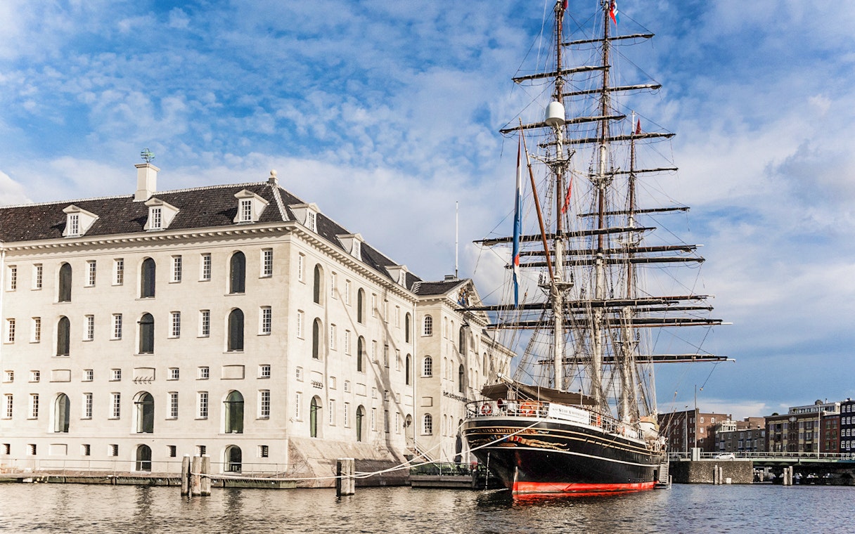National Maritime Museum in Amsterdam with historic ship docked nearby.