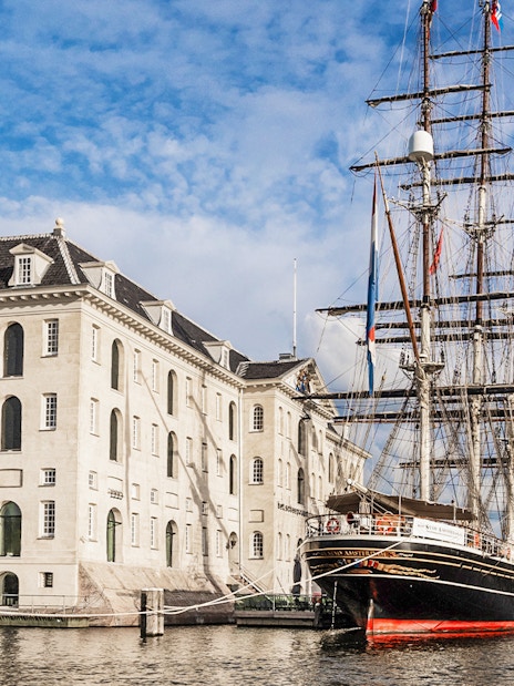 National Maritime Museum in Amsterdam with historic ship docked nearby.